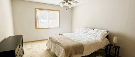 A bedroom with a bed, a ceiling fan, a window, a dresser, and a nightstand.