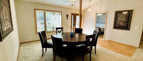 A dining area with a round table, chairs, a chandelier, and artwork on the walls.