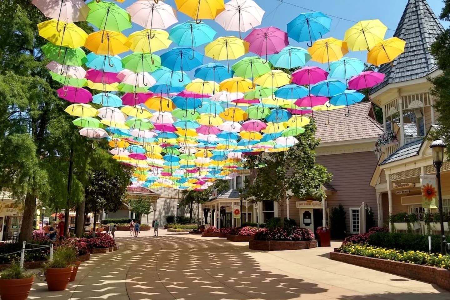 A street lined with buildings, a clear sky, and a canopy of colorful umbrellas.