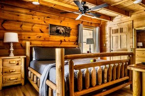Ein Schlafzimmer in einer Blockhütte mit einem hölzernen Bett, einem Deckenventilator, einem Fenster und einer Lampe.