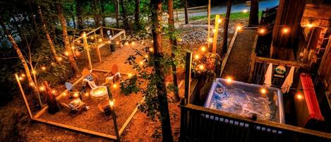 Una terraza de madera con un jacuzzi, luces cálidas y mobiliario exterior.