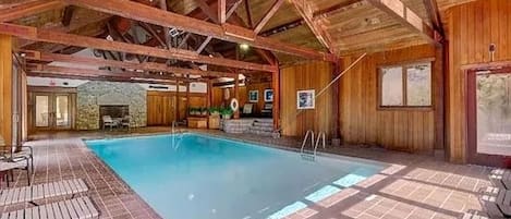 An indoor swimming pool with wooden beams, a stone wall, and a fireplace.