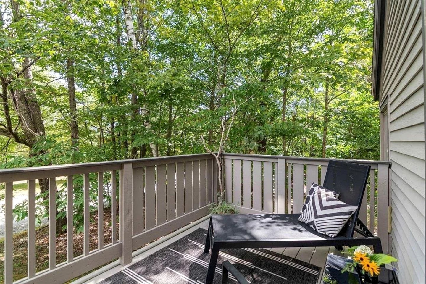 A wooden deck with a black chair and a small table, surrounded by trees.