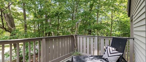 A wooden deck with a black chair and a small table, surrounded by trees.