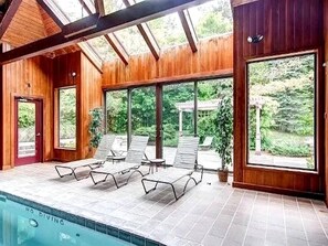 Un área de piscina con sillones reclinables, paredes de madera y grandes ventanales.