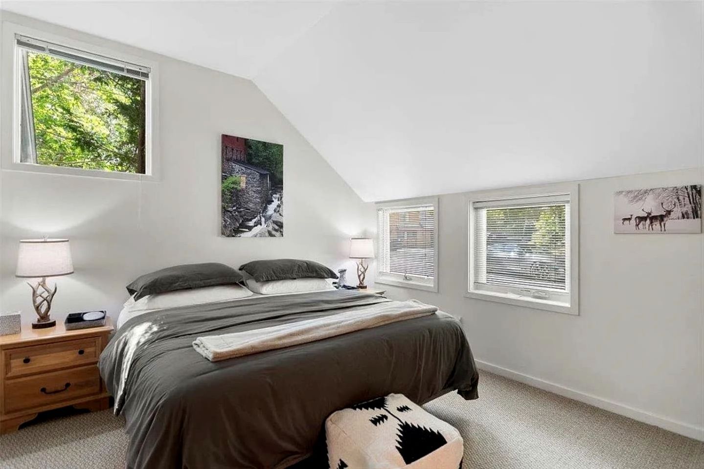 A bedroom with a bed, two bedside tables, a nightstand, a window with blinds, and a wall-mounted picture.