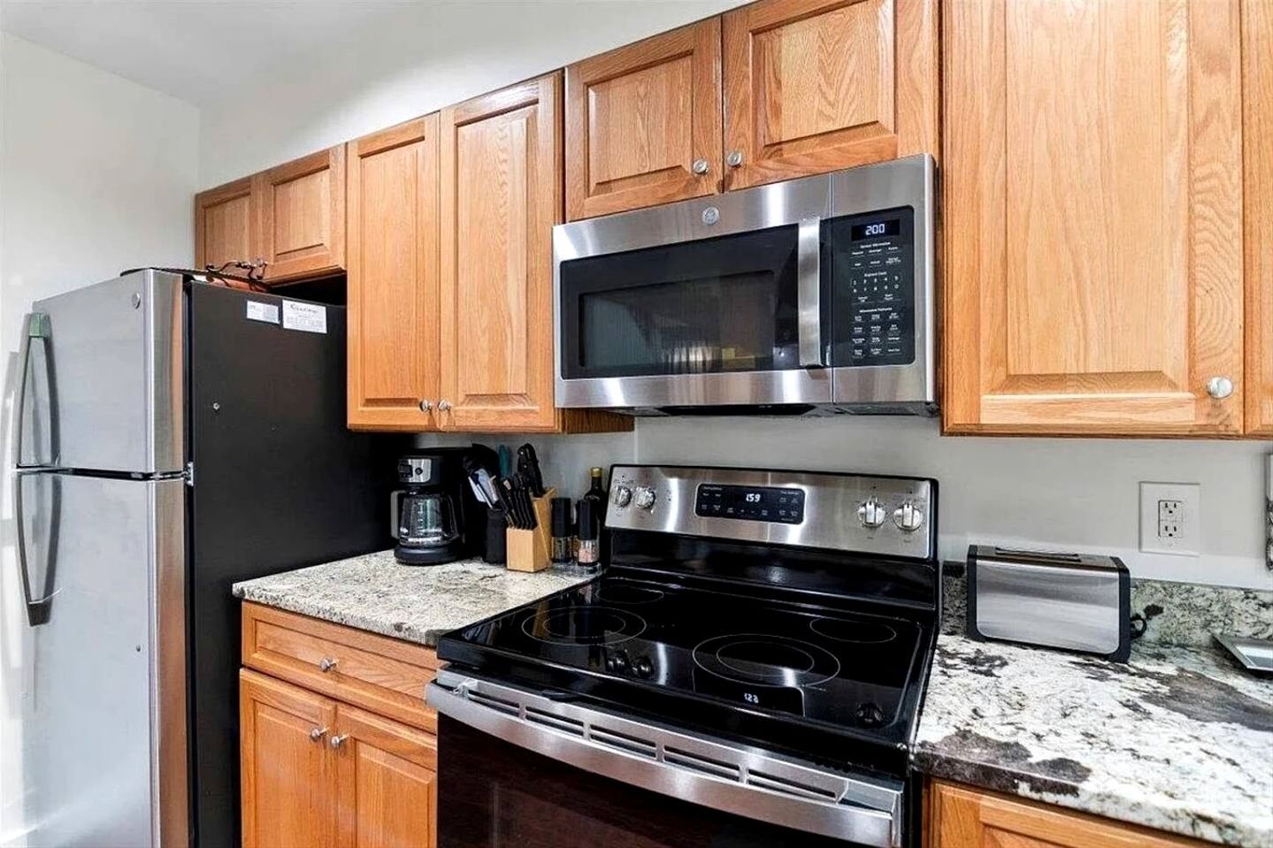 A kitchen with wooden cabinets, a stainless steel refrigerator, a microwave, a stove, and a coffee maker.