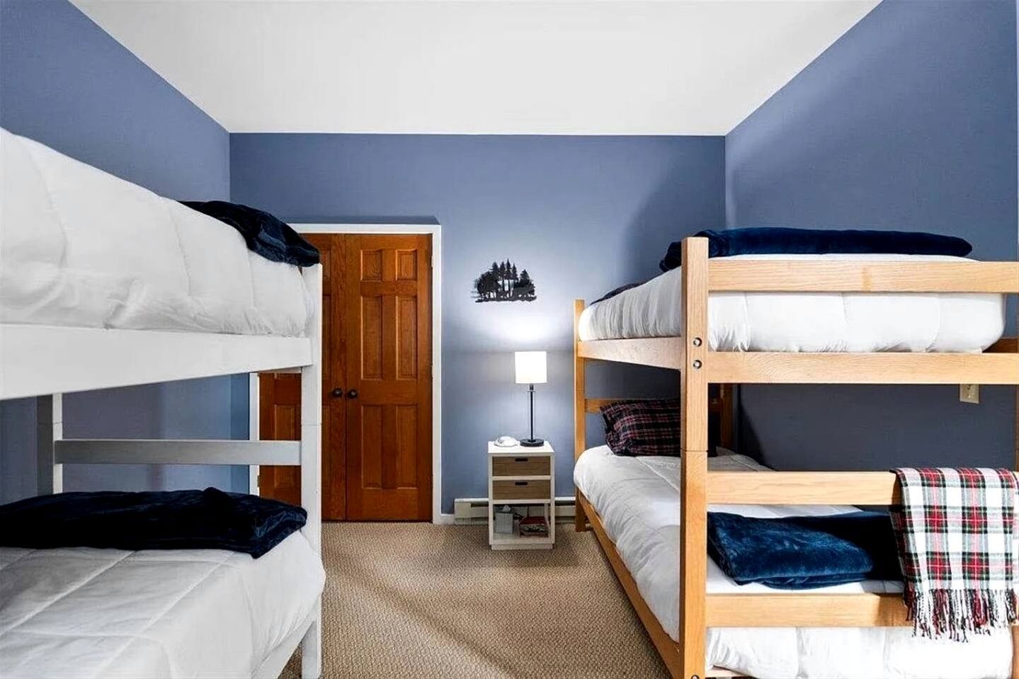 Ein Zimmer mit Etagenbetten, einer Tür, einem Nachttisch mit Lampe und einer Wanddekoration.