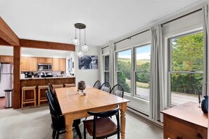 Eine geräumige Küche mit Holzausstattung, ein Essbereich mit großem Tisch und Stühlen sowie große Fenster mit Blick ins Freie.