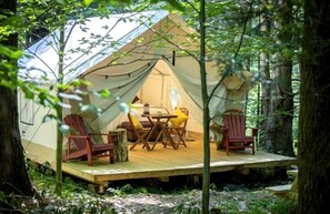A tent with a wooden deck, two chairs, a table, and a lamp.