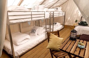 A bunk bed room with a wooden floor, a small table with a lantern, and a chair. - Glamping in New York in Fully-Equipped Safari Tents Located in Broadalbin (Broadalbin)