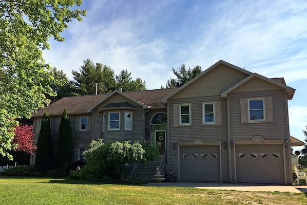 A two-story house with a front garage, a small front yard, and a tree with red leaves.