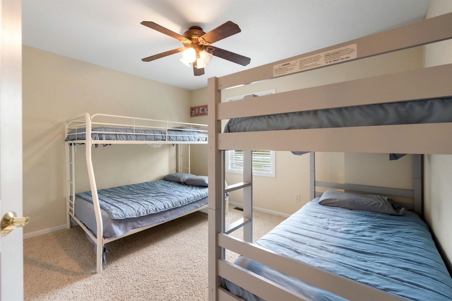 A room with two bunk beds, a ceiling fan, and a window with blinds.