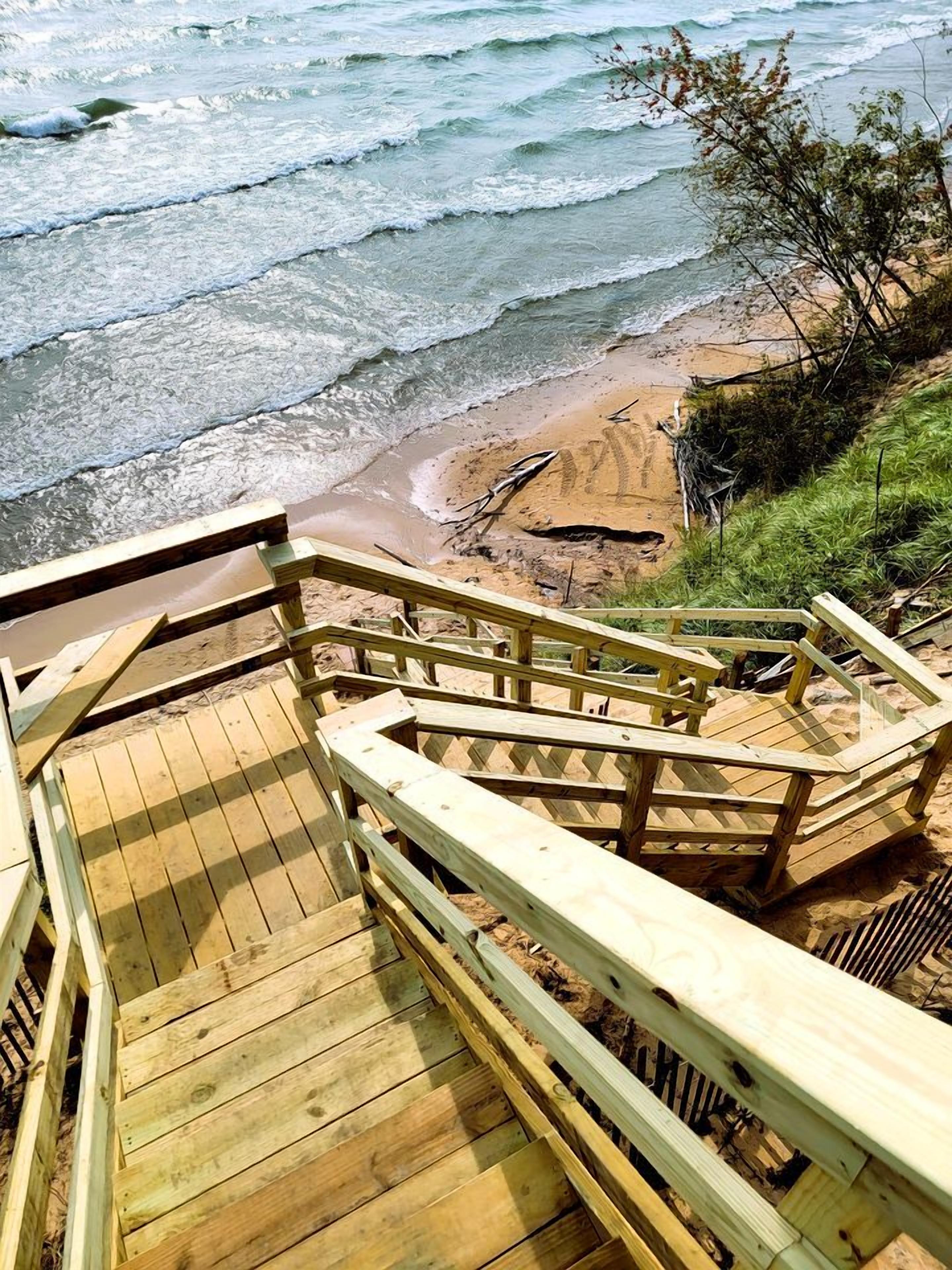 Een houten trap die naar een strand leidt, waar golven op het strand breken.