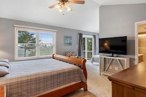 A bedroom with a bed, a TV, a ceiling fan, and a window with blinds.
