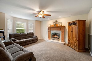 A living room with a fireplace, ceiling fan, and a large wooden cabinet.