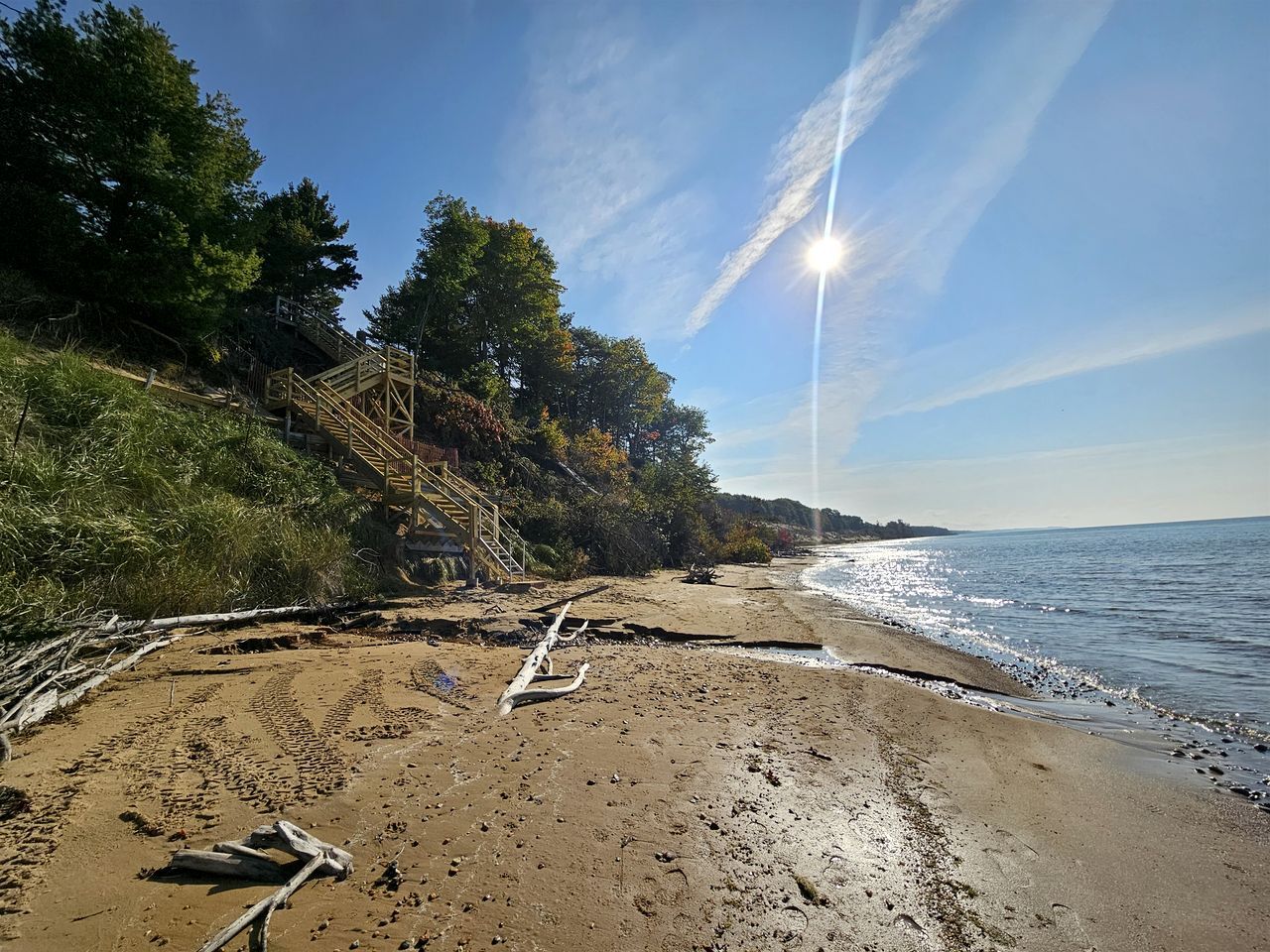 Una playa con una escalera de madera que baja hacia la orilla, rodeada de árboles y vegetación.