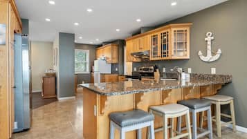 A kitchen with granite countertops, wooden cabinets, a stainless steel range, and a granite island with bar stools.