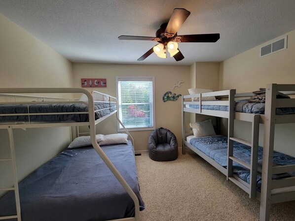 A room with bunk beds, a ceiling fan, a window with blinds, and a bean bag chair.