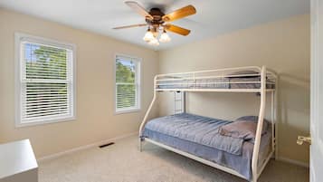 A bunk bed room with a ceiling fan, two windows with blinds, and a carpeted floor.