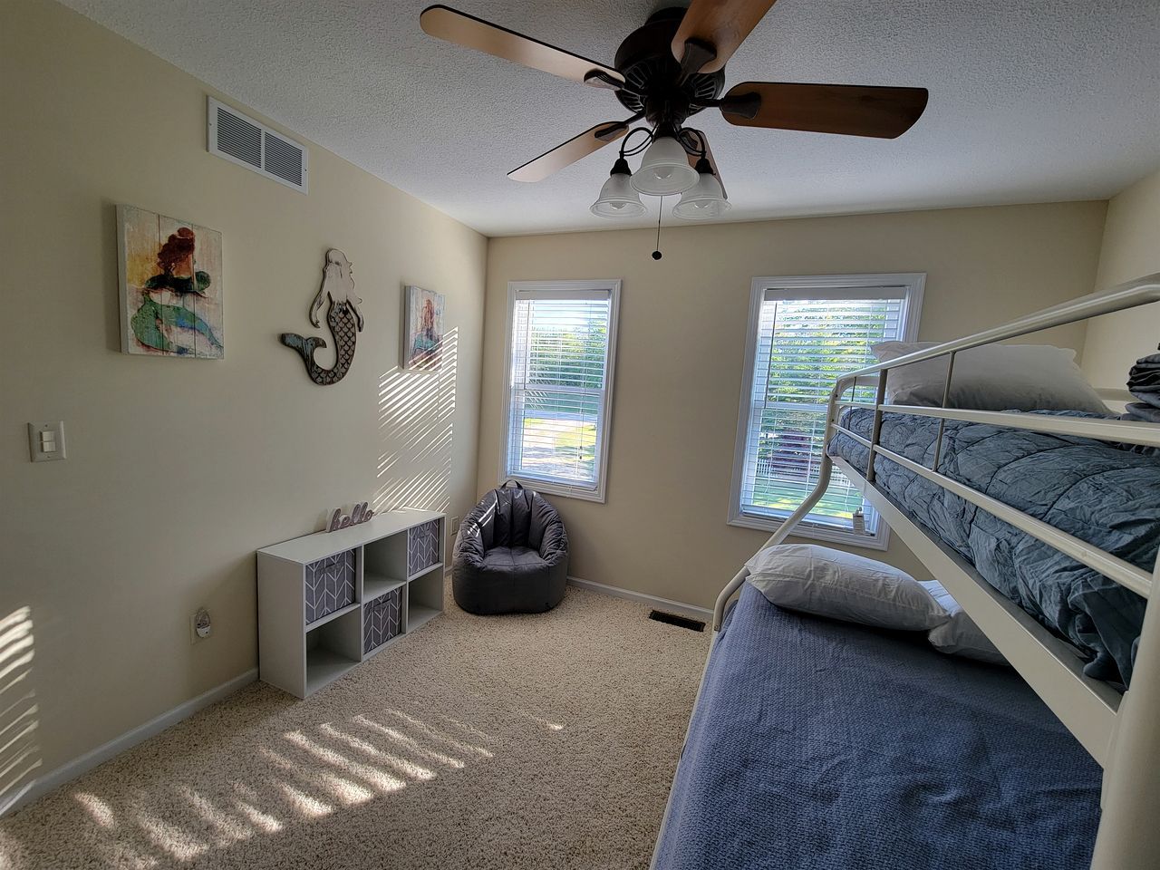 A bedroom with bunk beds, a ceiling fan, a bean bag chair, and a window with blinds.