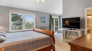 A bedroom with a bed, a TV, a ceiling fan, and a window with blinds.