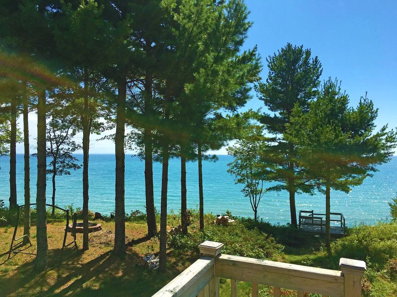 A wooden deck with a bench, overlooking a body of water with trees in the background.