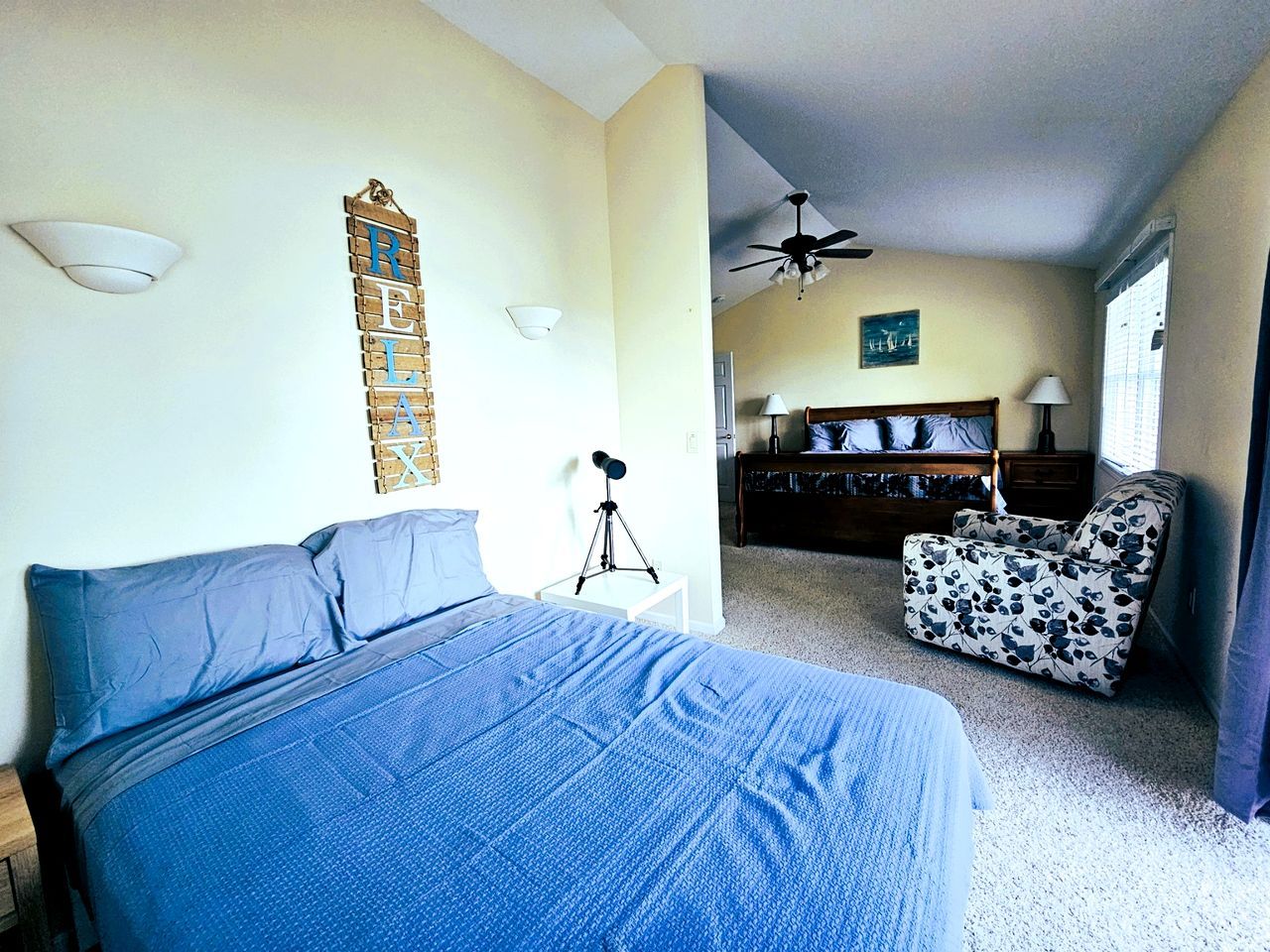 A bedroom with a bed, a desk, a chair, a ceiling fan, and a wall-mounted light fixture.