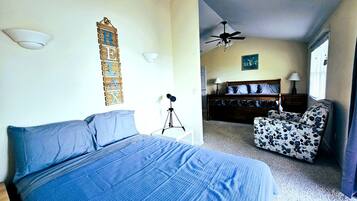 A bedroom with a bed, a desk, a chair, a ceiling fan, and a wall-mounted light fixture.