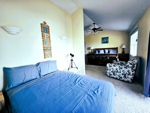 A bedroom with a bed, a desk, a chair, a ceiling fan, and a wall-mounted light fixture.
