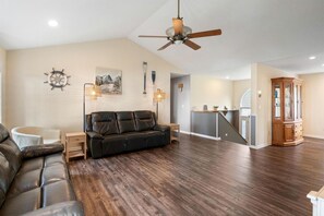 Un salon spacieux avec un canapé en cuir noir, un plancher en bois, un ventilateur de plafond et un meuble en bois.