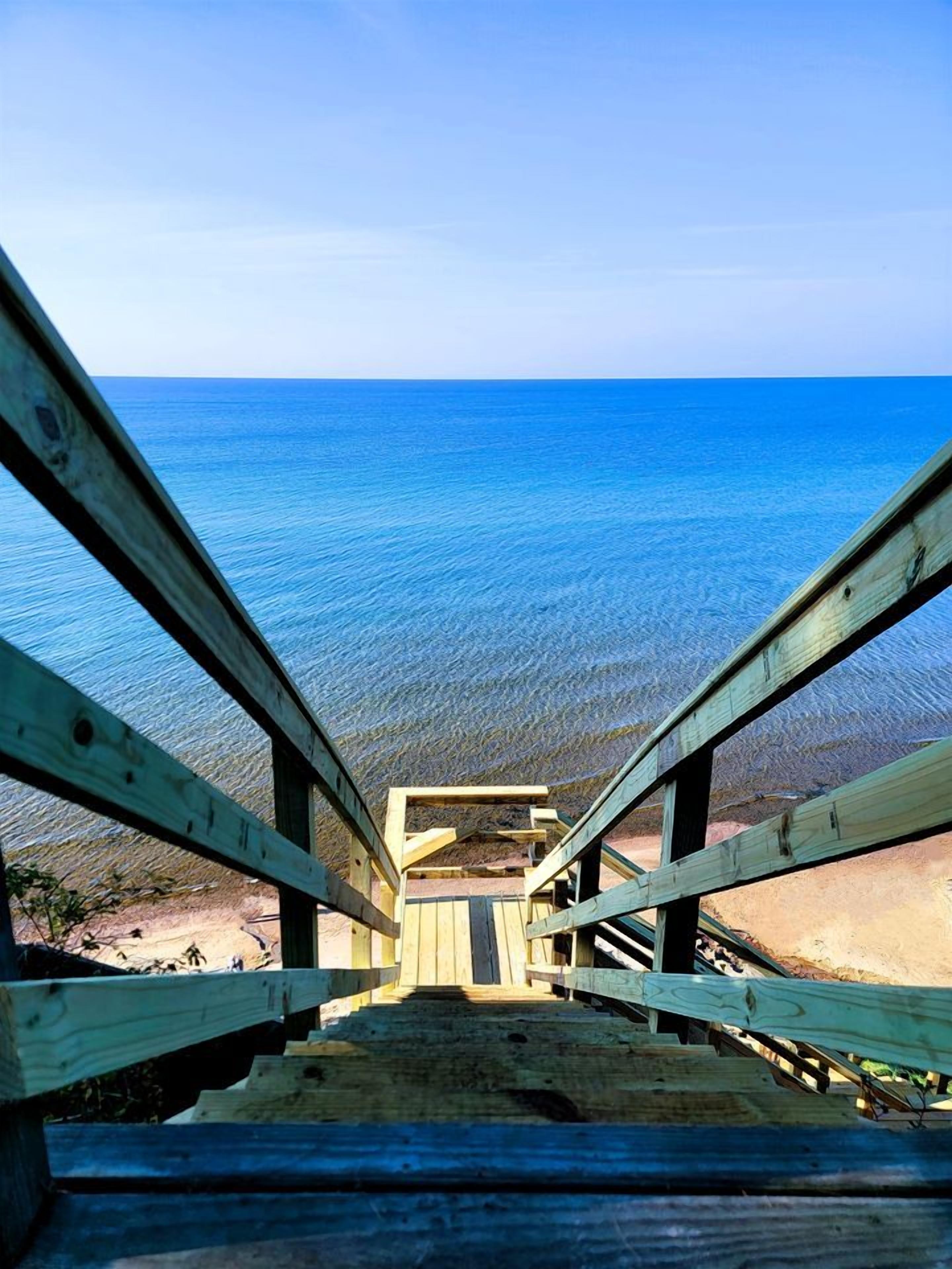 Un escalier en bois mène à une plage où l’eau est d’un bleu cristallin.