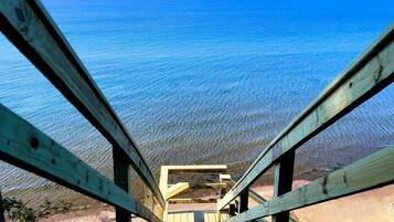 Un escalier en bois mène à une plage où l’eau est d’un bleu cristallin.