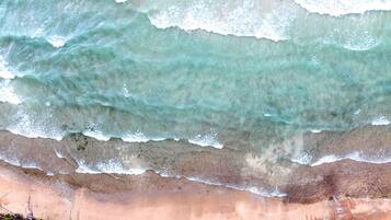 Ein Strand mit Wellen, Sand und vereinzelter Vegetation.