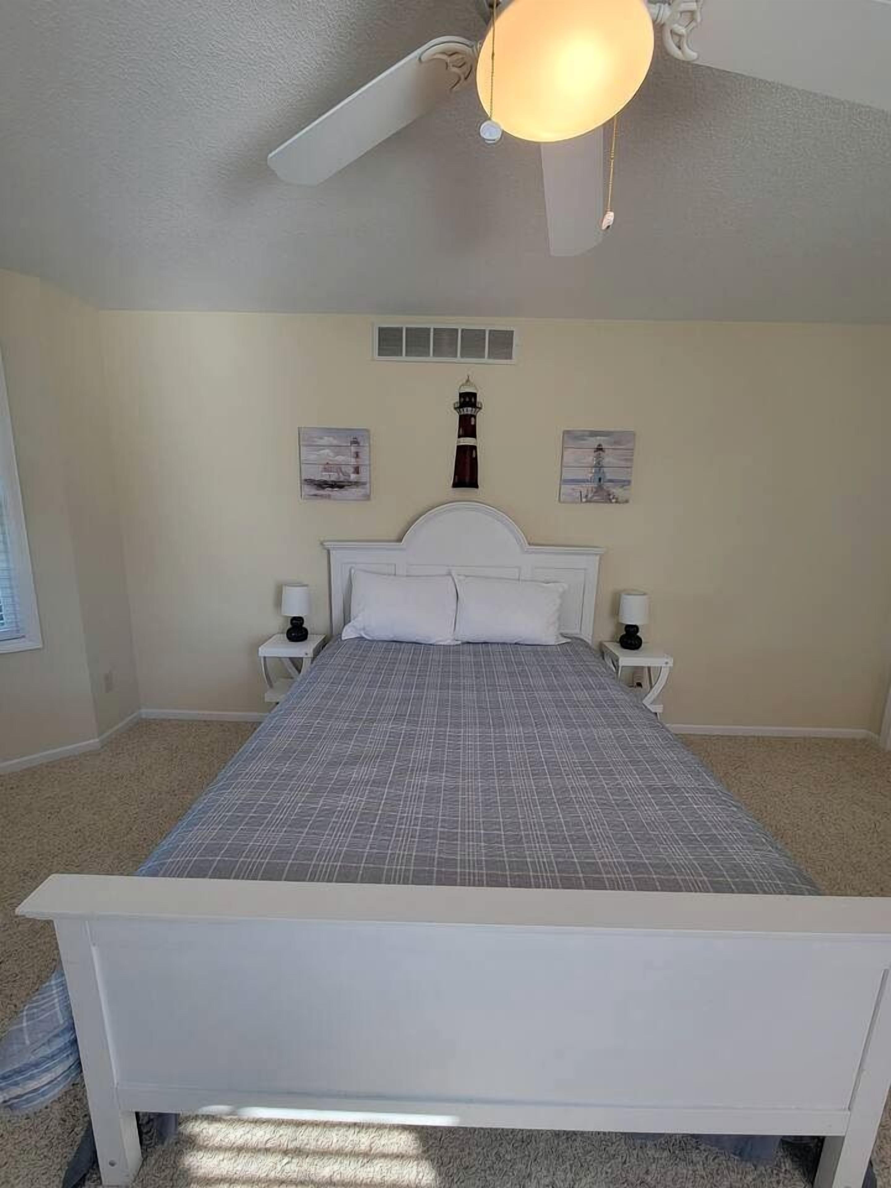 Quarto com cama, duas mesas de cabeceira, ventilador de teto e obras de arte nas paredes.