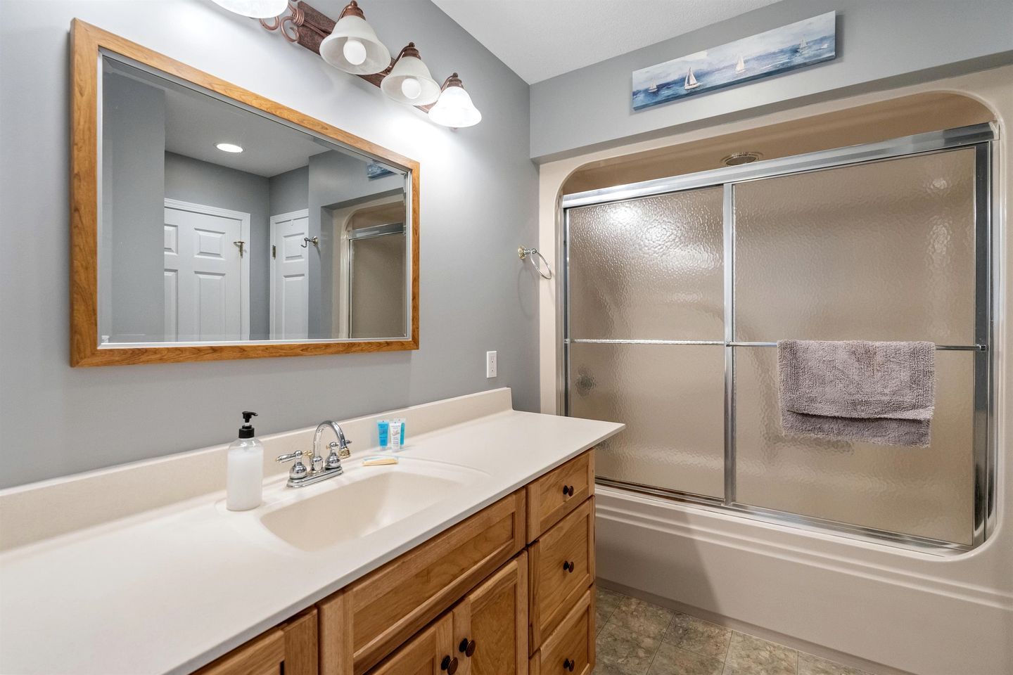 A bathroom with a large mirror, a sink, a shower, and wooden cabinets.
