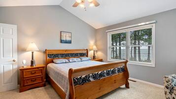 Une chambre à coucher avec un lit en bois, deux tables de chevet avec des lampes, un ventilateur de plafond, une fenêtre avec des stores et une porte.
