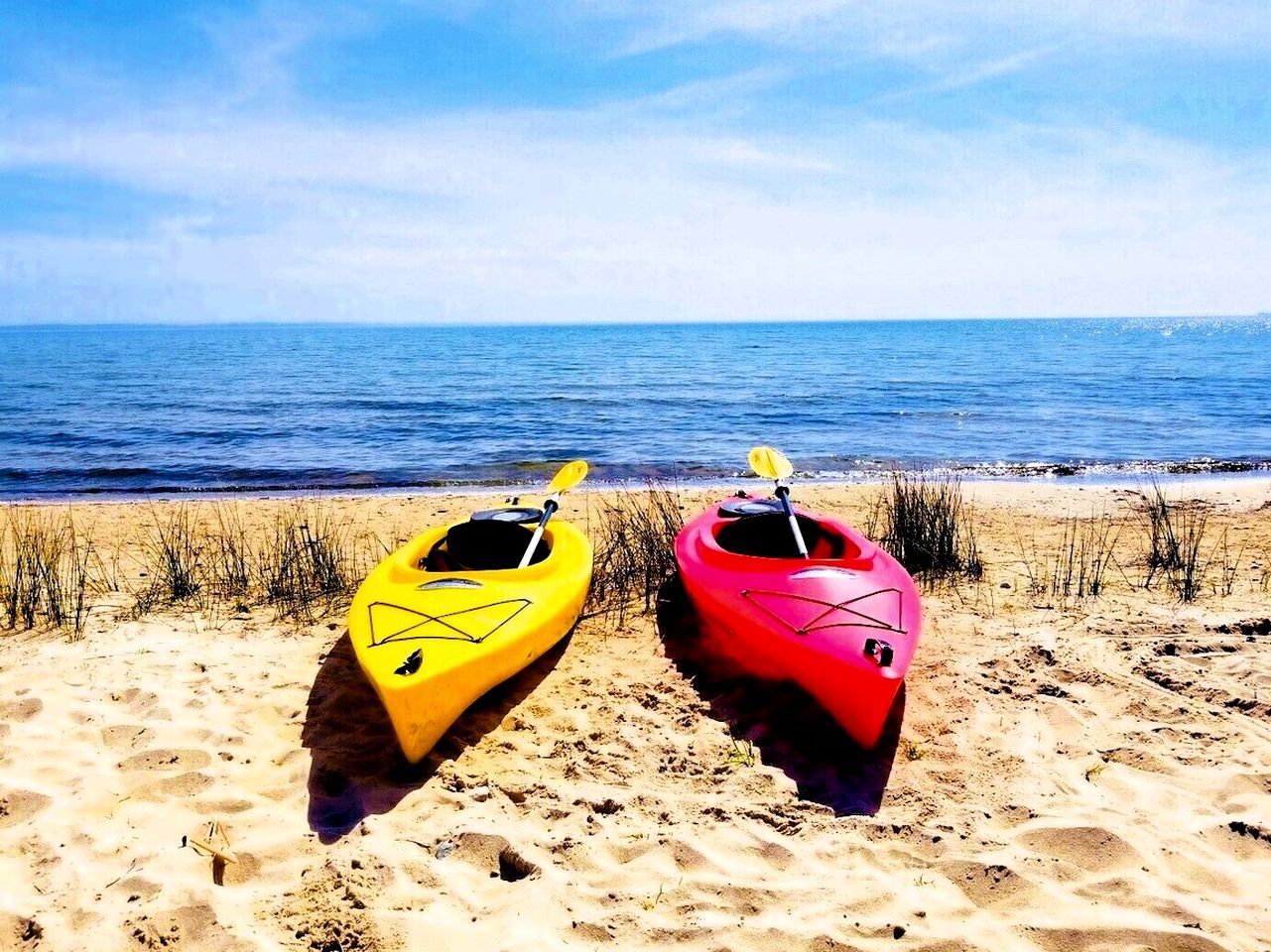 Dos kayaks en una playa arenosa con el océano al fondo.