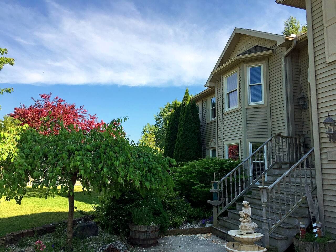 Ein Haus mit Veranda, Treppe und Garten, inklusive Baum und Vogeltränke.