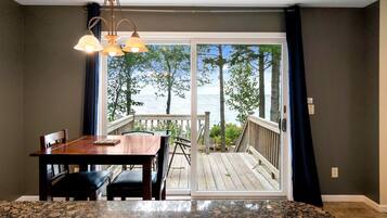 Un coin repas avec une table et des chaises, une vue sur la mer par une porte-fenêtre coulissante et une terrasse en bois à l’extérieur.