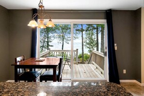 A dining area with a table and chairs, a view of the sea through a sliding glass door, and a wooden deck outside.