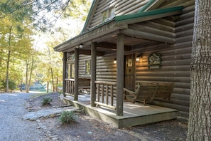 A log cabin with a porch, a sign indicating breakfast service, and a view of the surrounding forest.