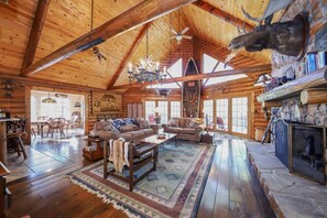 A log cabin interior with a high ceiling, wooden floors, a fireplace, and a dining area.