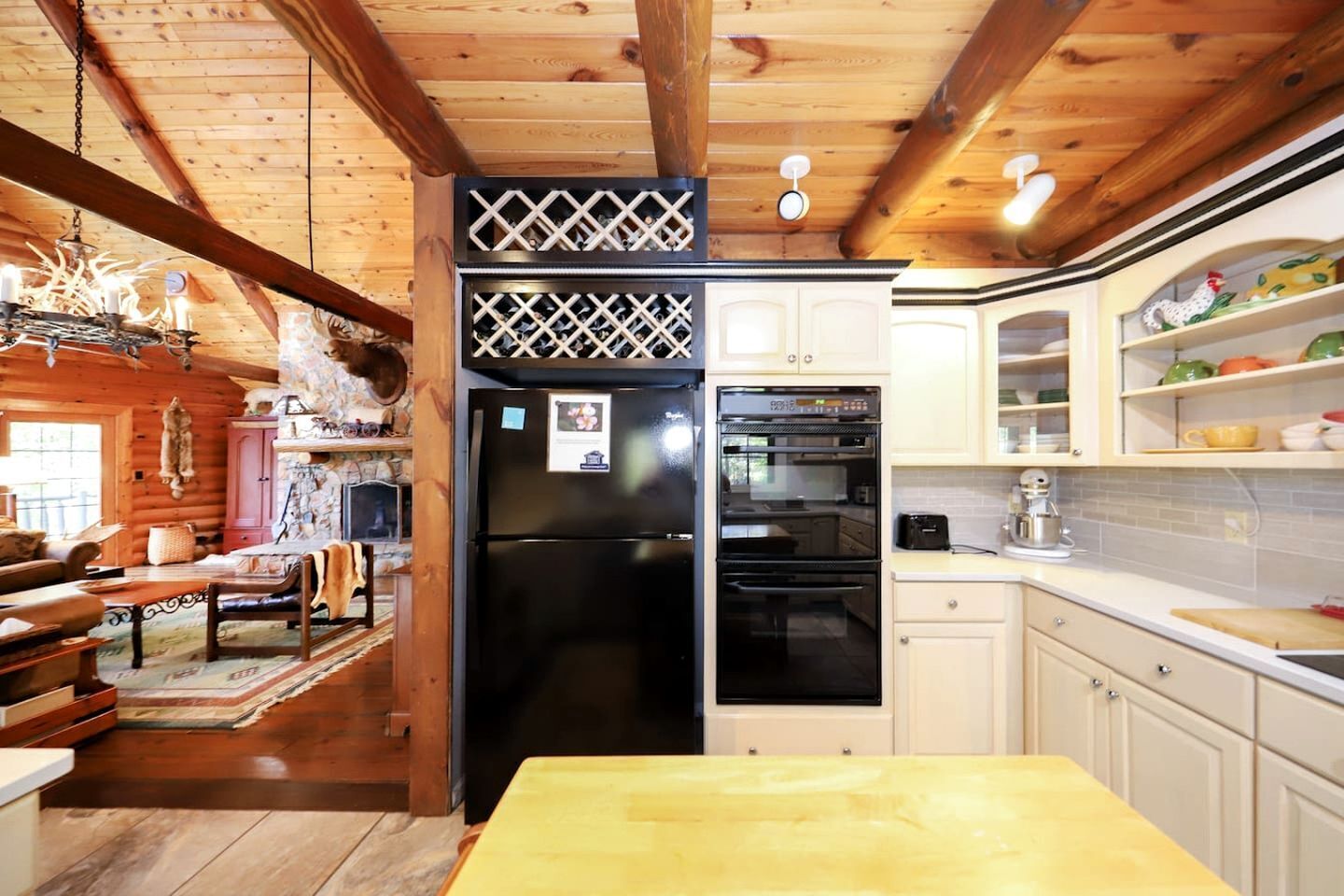 A log cabin interior with a wooden dining table, a kitchen with white cabinets, a black refrigerator, and a built-in oven.
