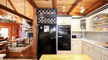 A log cabin interior with a wooden dining table, a kitchen with white cabinets, a black refrigerator, and a built-in oven.