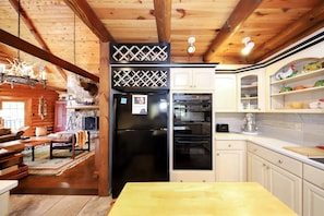 A log cabin interior with a wooden dining table, a kitchen with white cabinets, a black refrigerator, and a built-in oven.