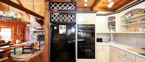 A log cabin interior with a wooden dining table, a kitchen with white cabinets, a black refrigerator, and a built-in oven.