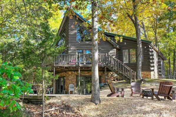 A log cabin with a balcony, a stone foundation, and a staircase leading to the main entrance.