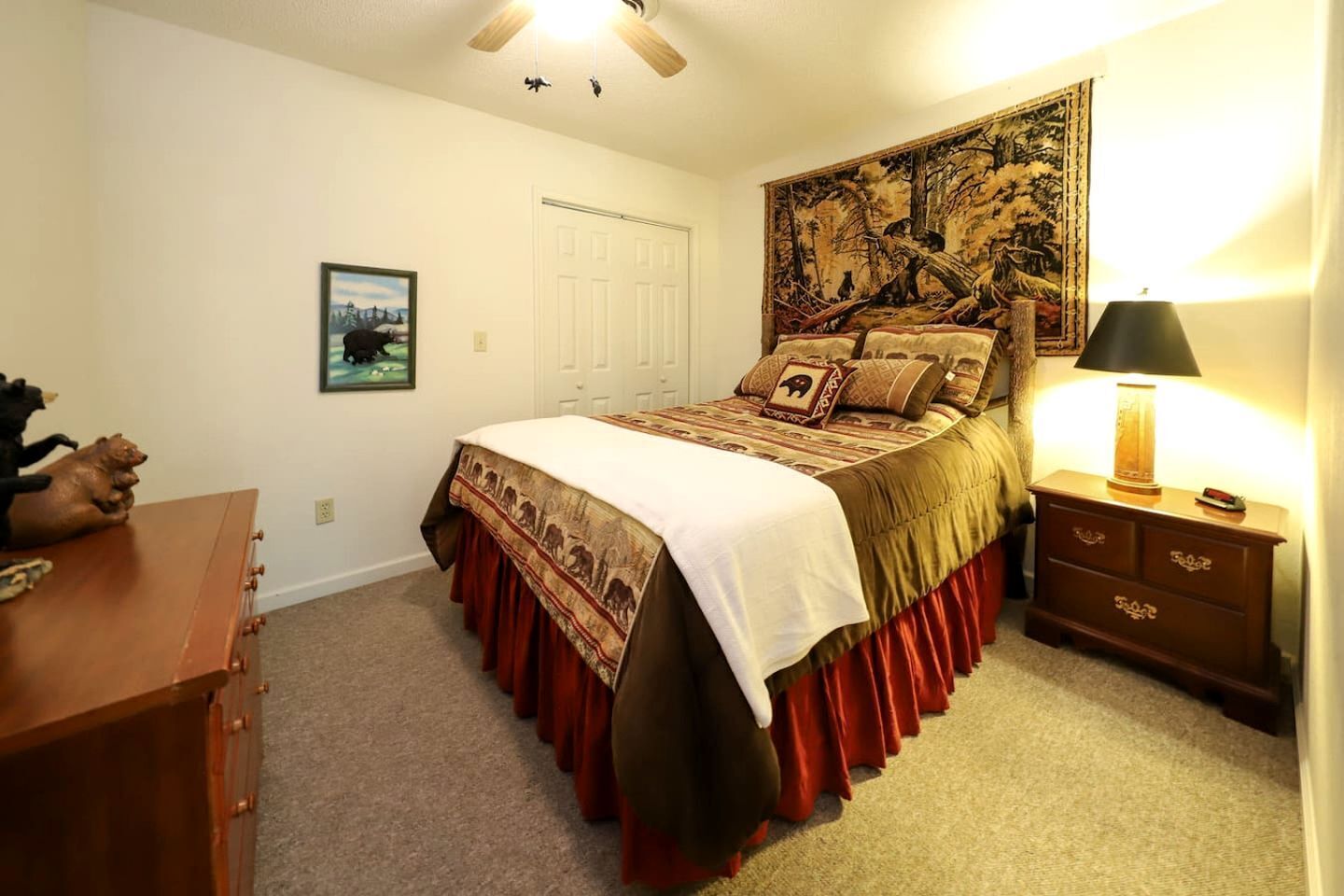 A bedroom with a bed, a nightstand, a dresser, a tapestry, a door, and a framed picture on the wall.