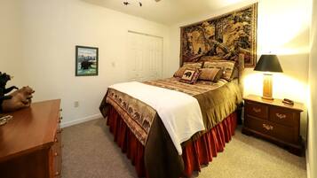A bedroom with a bed, a nightstand, a dresser, a tapestry, a door, and a framed picture on the wall.